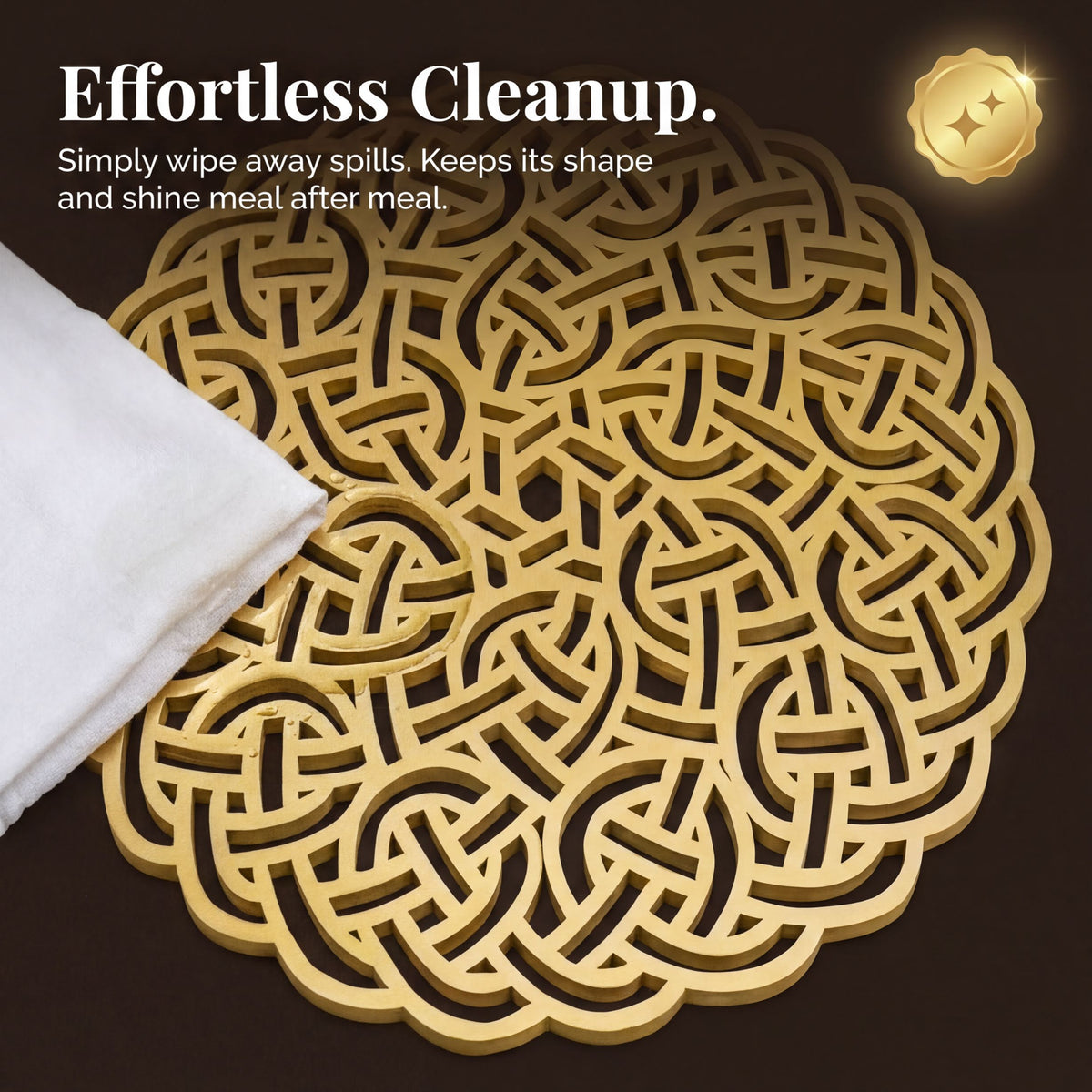 a decorative golden coaster with an intricate, woven pattern. The coaster is placed on a dark surface, and there is a white cloth or napkin next to it. The caption below the image reads "Effortless Cleanup. Simply wipe away spills. Keeps its shape and shines meal after meal."
