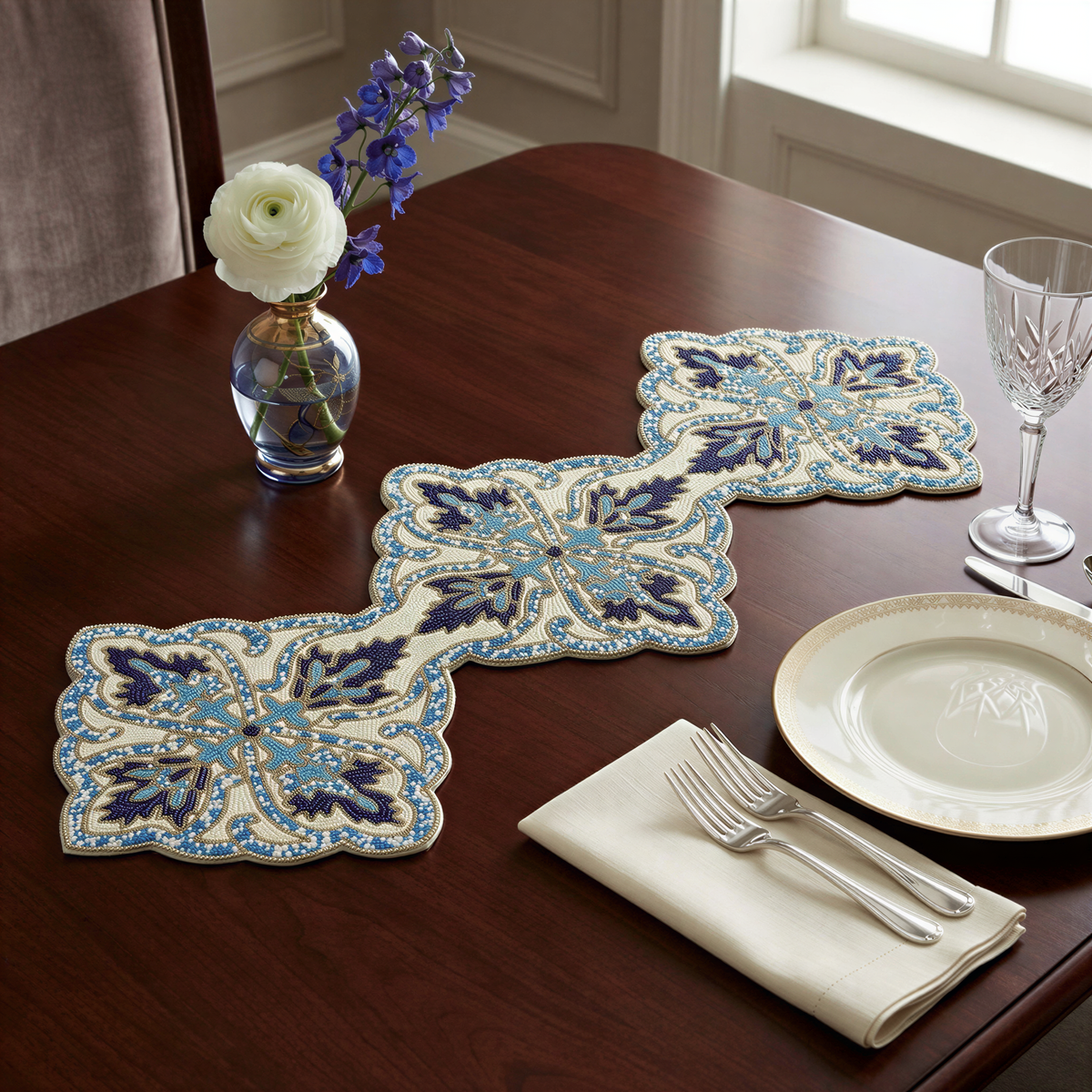 a table setting with a vase of white roses, a blue and white patterned runner, a plate, a fork, and a knife.