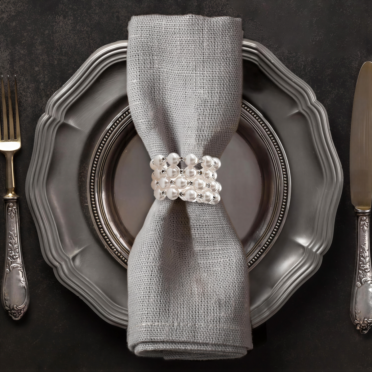 A silver dinner plate with a napkin ring and silverware, including a fork and knife, arranged on a dark surface.
