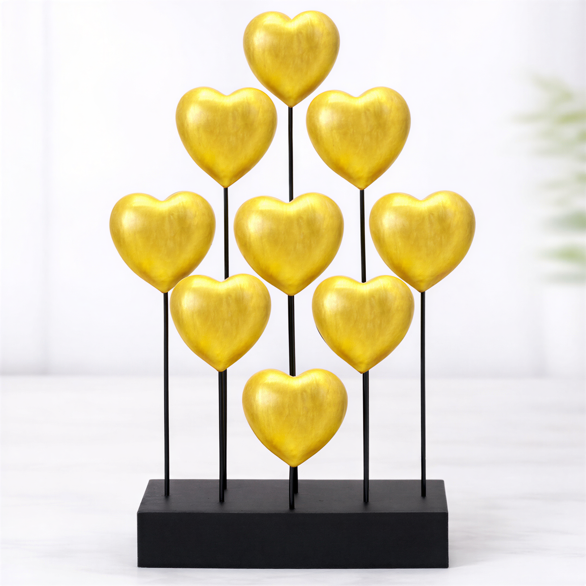 A display of nine golden heart-shaped objects arranged in a pyramid-like structure on a black base.