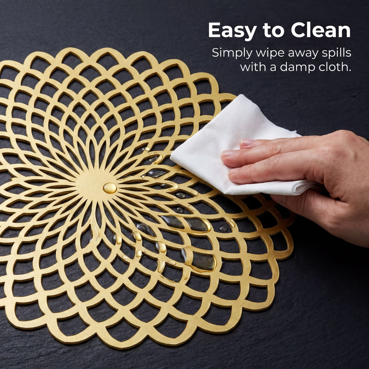 A hand is wiping a gold-colored, intricate, and textured placemat with a damp cloth, as described in the image caption.