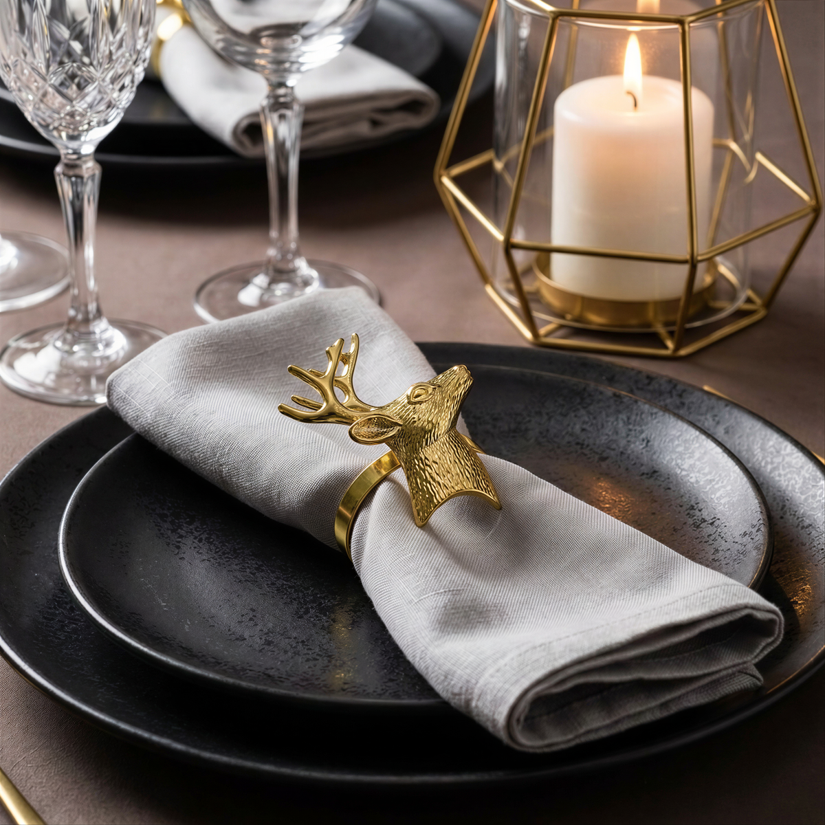 a table setting with a black plate, a white napkin, and a gold-colored decorative piece featuring a deer head. There are also wine glasses and a lit candle in the background, creating a cozy and elegant atmosphere.