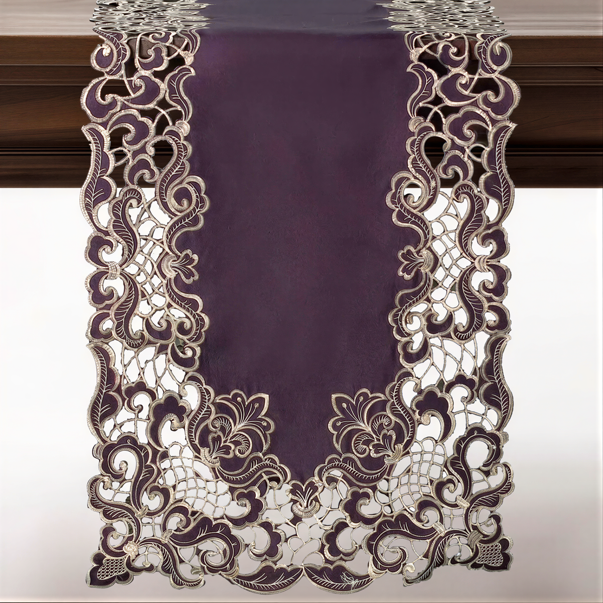 a purple table runner with an intricate, lace-like design. The design is predominantly purple and white, with a floral pattern that adds a touch of elegance to the runner. The runner is hanging on a wooden surface, creating a visually appealing and decorative display.