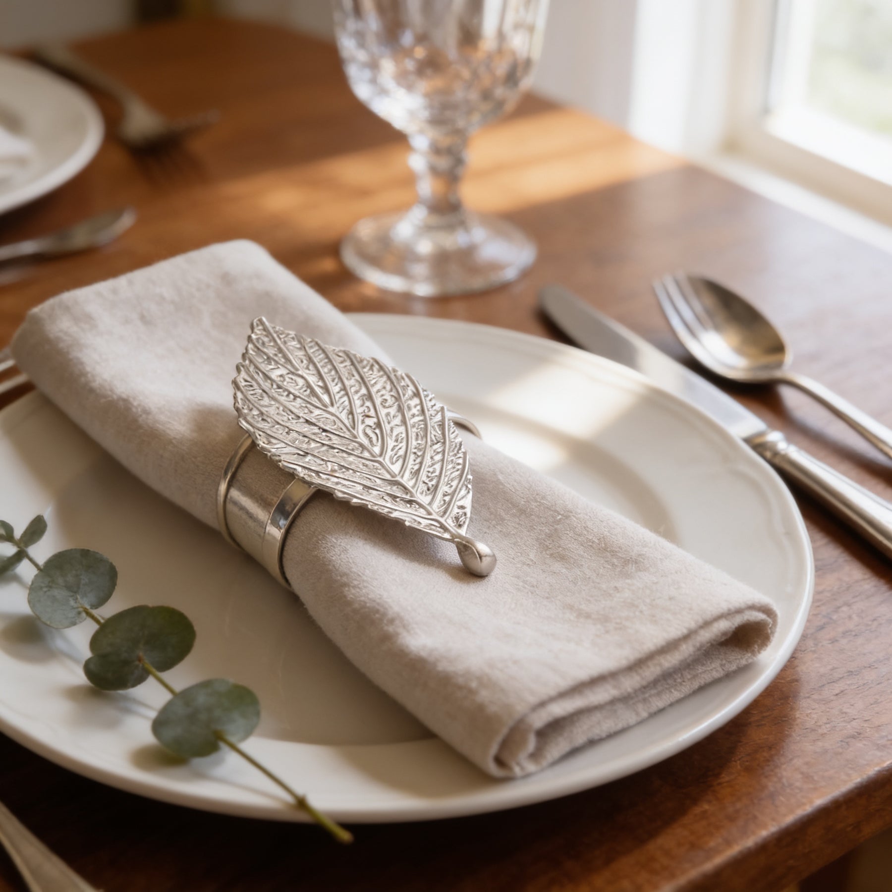 A white plate with a napkin rolled up in a napkin ring, silverware, and a glass of water on a wooden table.