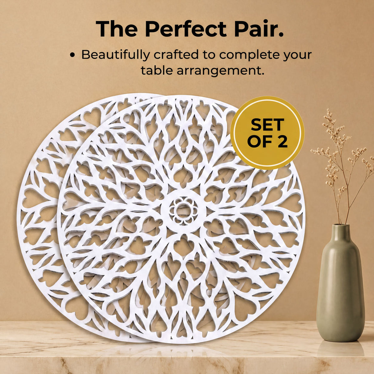 a set of two white, circular wall art pieces with a floral design, placed on a marble surface next to a vase with dried flowers.