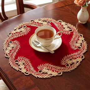 A cup of tea sits on a red and gold place mat, accompanied by a small vase of flowers on a wooden table.