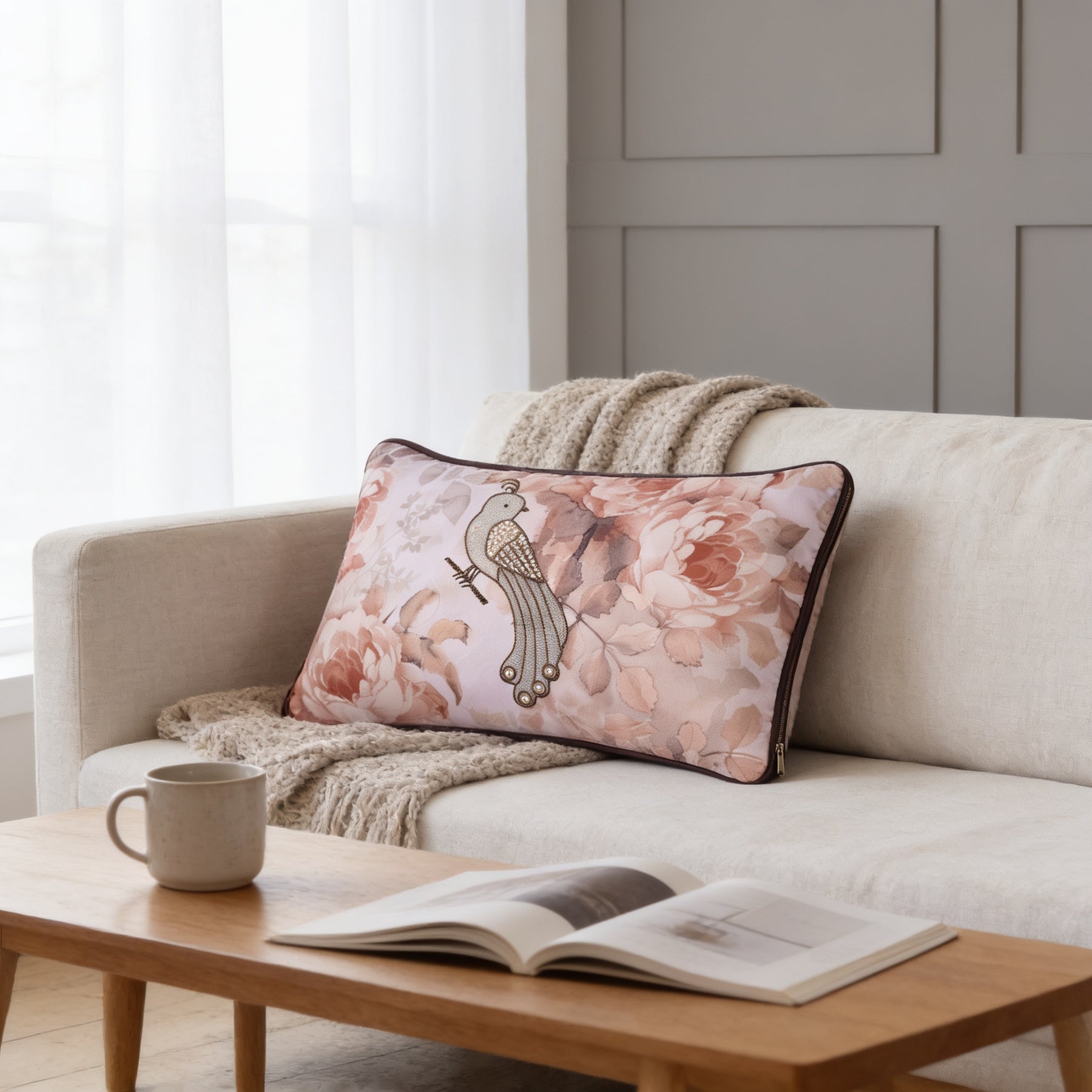 a cozy living room with a white sofa, a wooden coffee table, and a decorative pillow with a floral design. There is also a mug and an open book on the coffee table, creating a comfortable and inviting atmosphere.