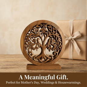 A wooden tree-shaped ornament with intricate carvings sits on a wooden surface, accompanied by a gift box with a white ribbon tied around it.