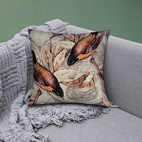 A decorative throw pillow with a bird design sits on a gray couch, partially covered by a gray blanket.