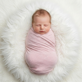 A newborn baby swaddled in a pink blanket is peacefully sleeping on a white fluffy surface.