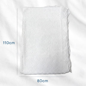 a white knitted blanket or quilt with a pattern of small holes or dots. The blanket is folded and placed on a white surface, with measurements provided in centimeters.