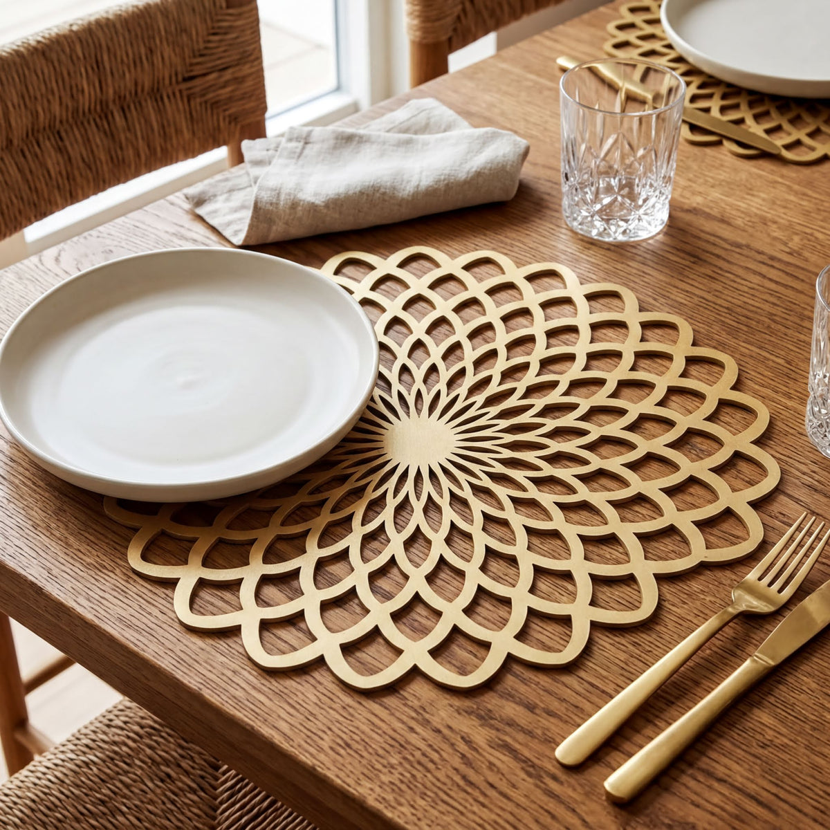 a table setting with a white plate, a gold floral placemat, and various tableware items such as a fork, knife, and a glass.