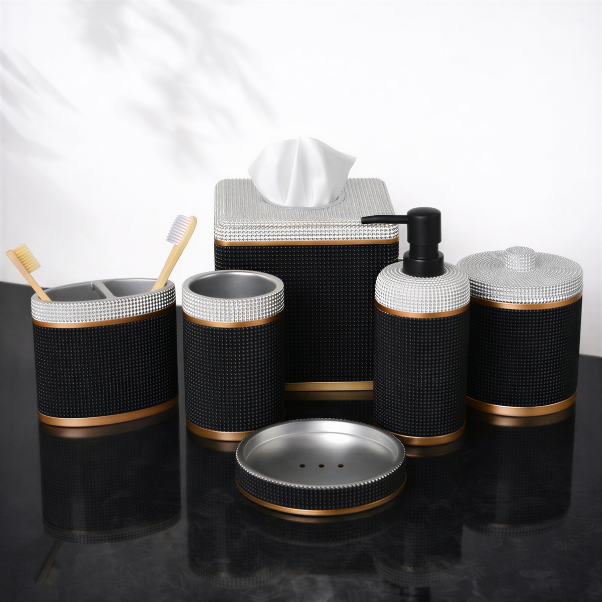 A set of black and gold bathroom accessories, including a tissue box, soap dispenser, toothbrush holder, and other small containers, arranged on a black surface.