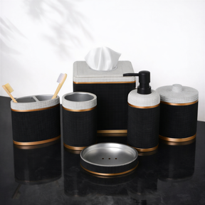 A set of black and gold bathroom accessories, including a tissue box, soap dispenser, toothbrush holder, and other small containers, arranged on a black surface.