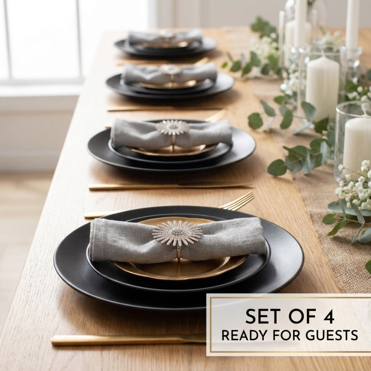 A set of four black plates with gold accents, each set with a folded napkin and a small decorative piece, arranged on a wooden table.