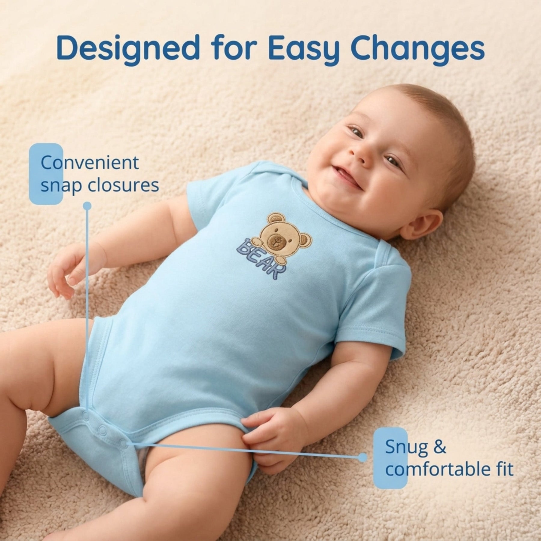 A smiling baby wearing a blue onesie with a teddy bear design lying on a carpeted floor.