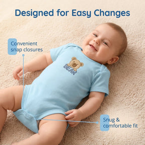A smiling baby wearing a blue onesie with a teddy bear design lying on a carpeted floor.