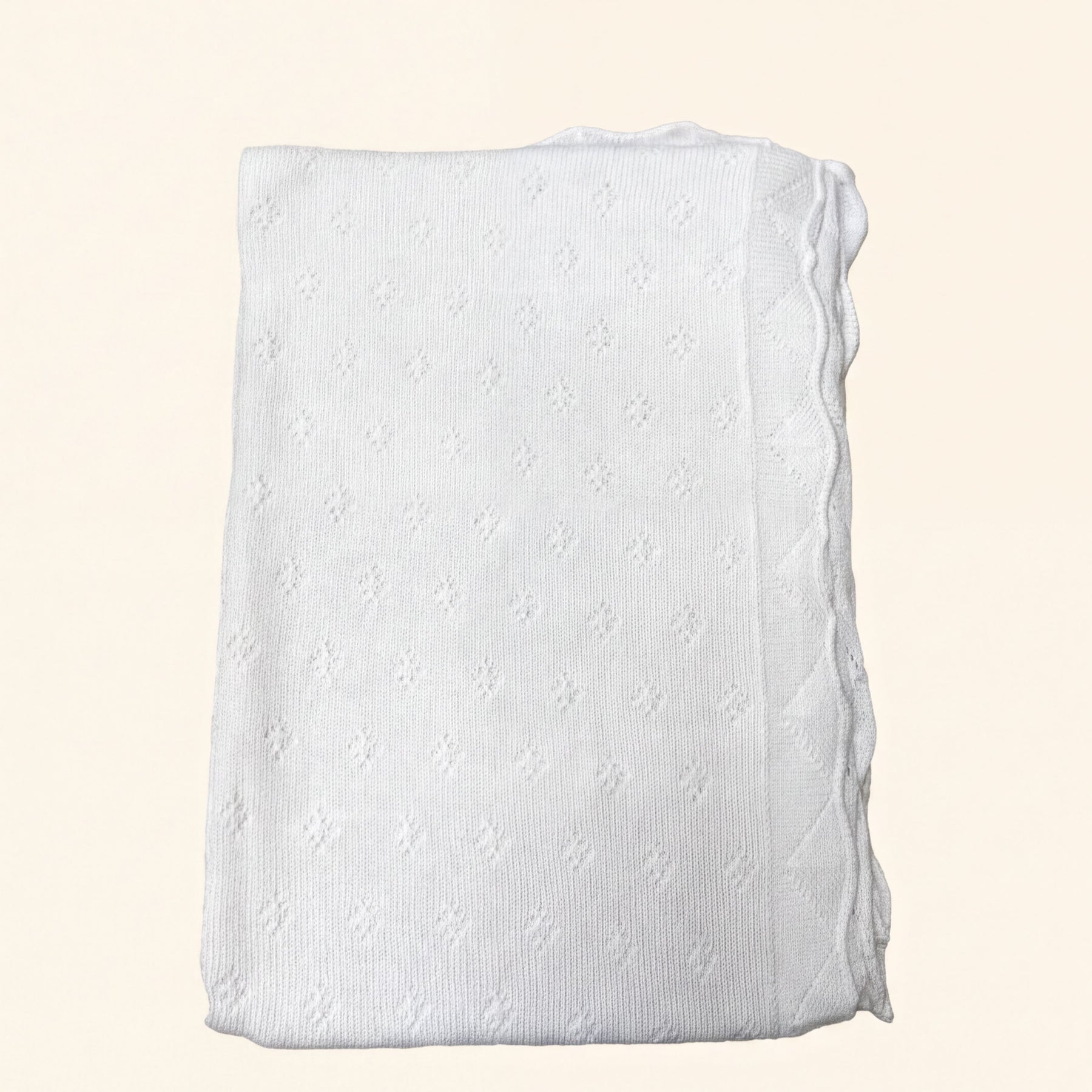 A white knitted blanket with a scalloped edge is shown against a light background.