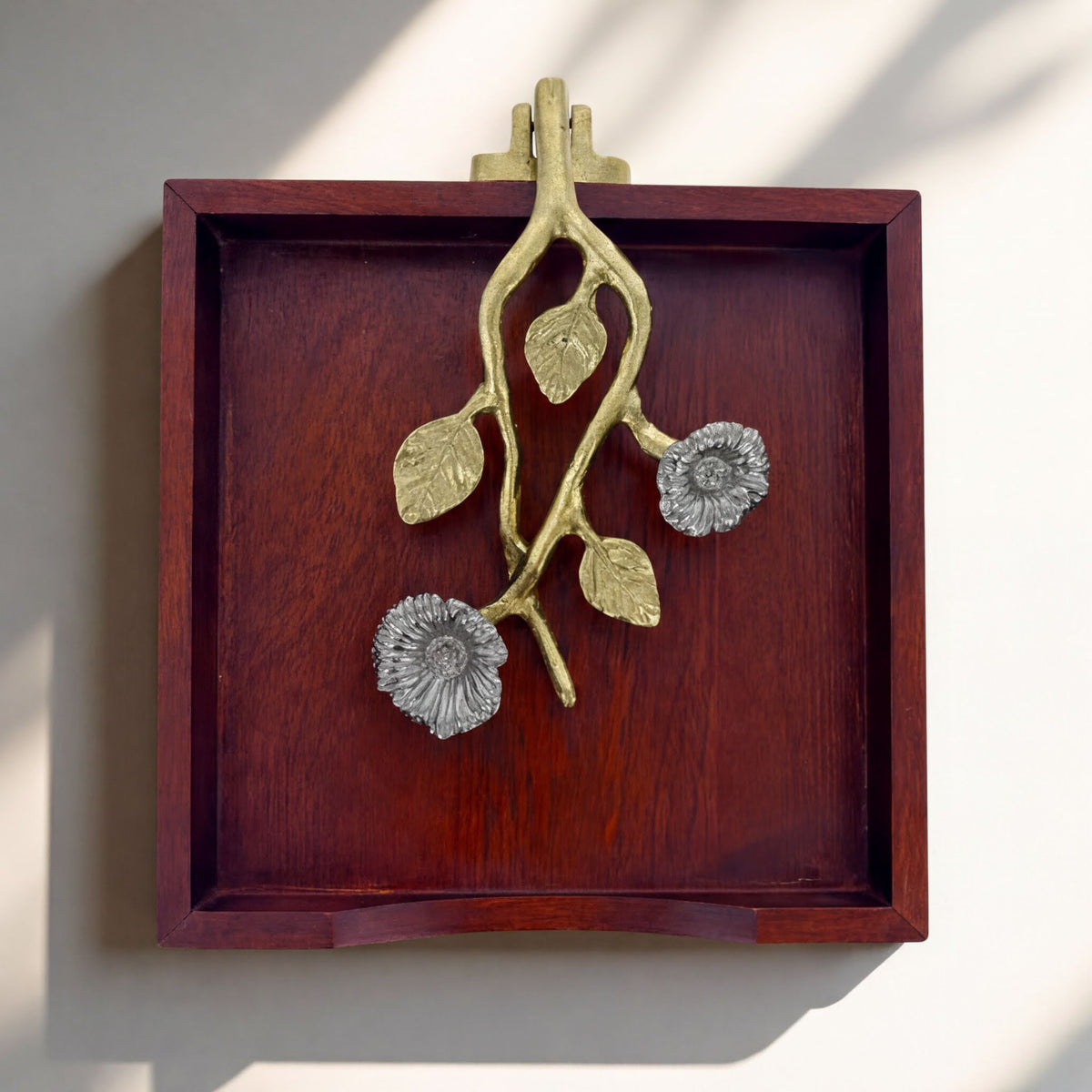 A wooden tray with a decorative metal piece featuring a branch with flowers on it.