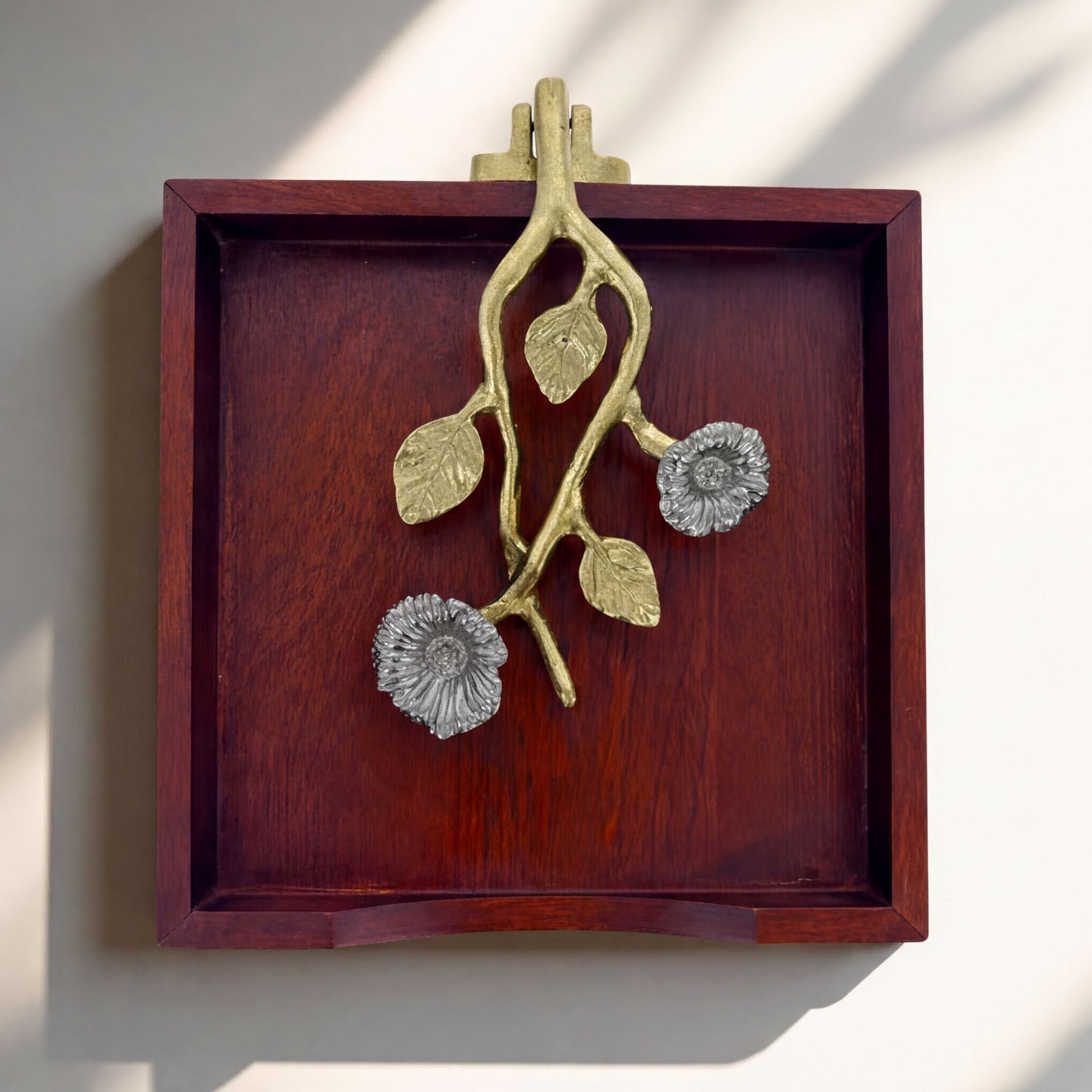 A wooden tray with a decorative metal piece featuring a branch with flowers on it.