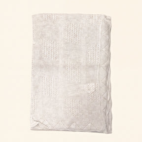 A cream-colored knitted blanket with a geometric pattern.