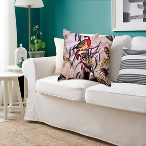 a living room with a white sofa adorned with a colorful, tropical-themed pillow. The room has a green wall, a white table, and a lamp, creating a cozy and inviting atmosphere.