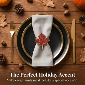 a table setting with a black plate, a gold rim, and a white napkin with a red maple leaf napkin ring. The table is decorated with autumn leaves, pine cones, and acorns.