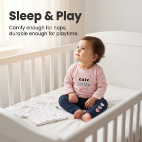 A baby girl sits in a crib, wearing a pink shirt with the words "cute little girl" and blue pants with three hearts.