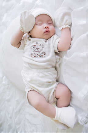 A sleeping baby dressed in a white outfit with a teddy bear design, lying on a white background.