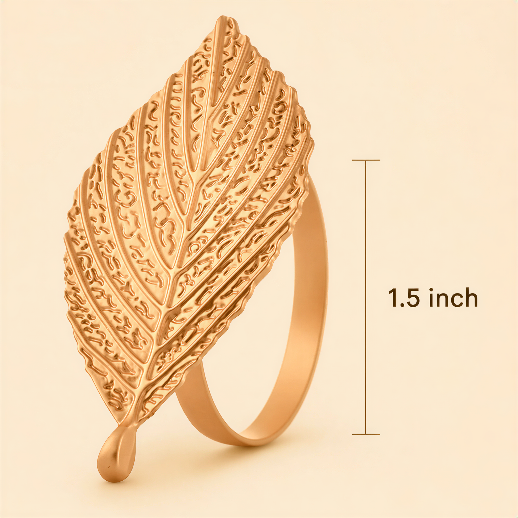 A gold leaf-shaped ring with a drop of liquid at the bottom, against a light beige background.