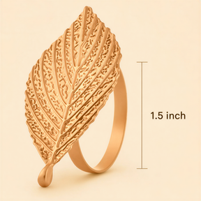 A gold leaf-shaped ring with a drop of liquid at the bottom, against a light beige background.