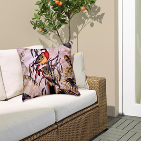 a cozy outdoor seating area with a white wicker sofa and a decorative pillow with a tropical bird design. The pillow is placed on the sofa, and there is a small tree with orange fruits growing next to it. The overall scene has a warm and inviting atmosphere.