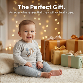 A smiling baby sitting on a carpet surrounded by wrapped gifts, with a background of twinkling lights.