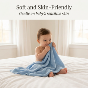 A smiling baby wrapped in a soft blue blanket sits on a bed, looking content and comfortable.