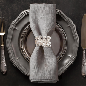 A silver dinner plate with a napkin ring and silverware, including a fork and knife, arranged on a dark surface.