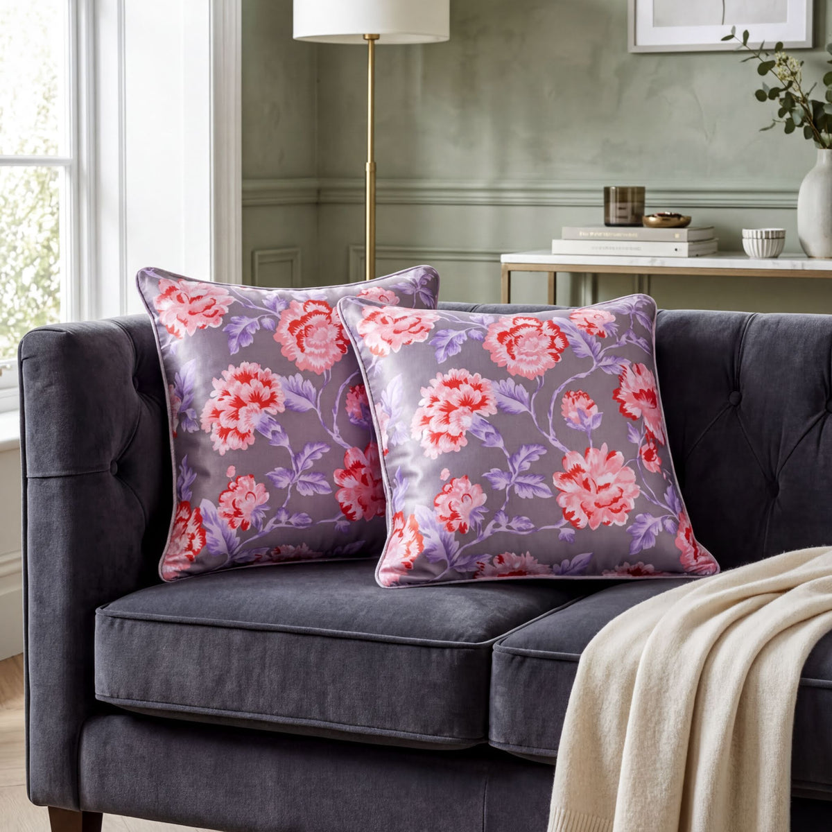 a cozy living room with a gray sofa adorned with two matching floral throw pillows in shades of purple and pink. The pillows are placed on the sofa, creating a visually appealing and inviting atmosphere.