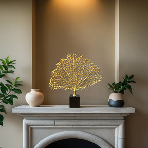 a white fireplace mantel with a decorative gold leaf sculpture and two small vases placed on it.