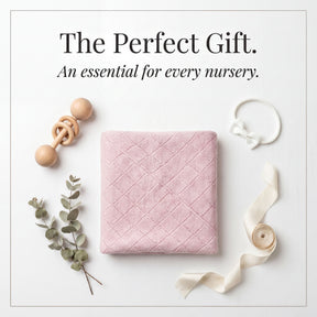a collection of baby-related items arranged on a white background, including a pink quilted blanket, a wooden baby rattle, a white bow, and some greenery.