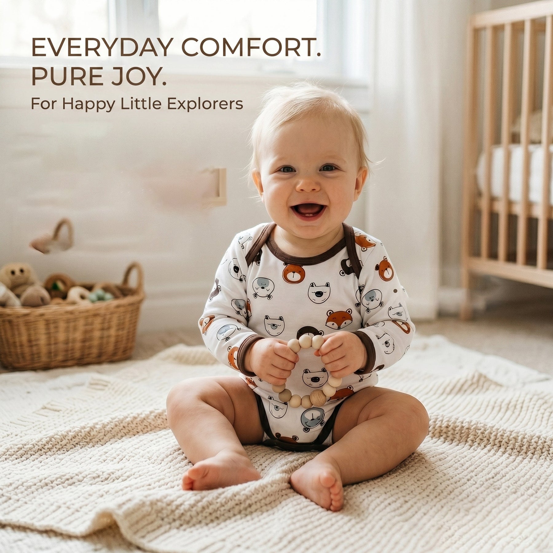 A smiling baby in a white onesie with animal prints sits on a white blanket, holding a wooden toy in their hands.