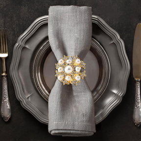 A silver dinner plate with a decorative napkin ring featuring a large, ornate piece of jewelry, likely a brooch or pendant, placed on top of it.