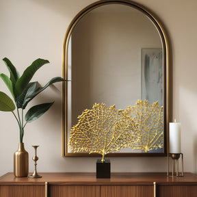 a wooden dresser with a gold-framed mirror, a plant, and a decorative golden leaf sculpture on top.