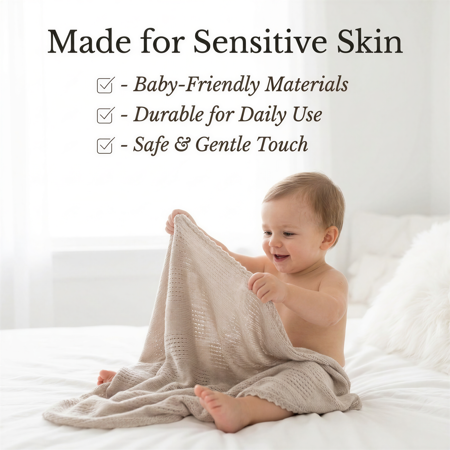 A smiling baby wrapped in a soft, beige blanket sits on a bed, holding the blanket with their hands.