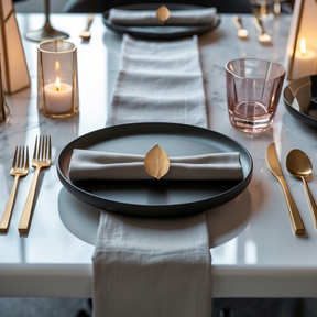 a beautifully set dining table with a black plate, gold-colored utensils, and a napkin ring with a leaf-shaped accent.