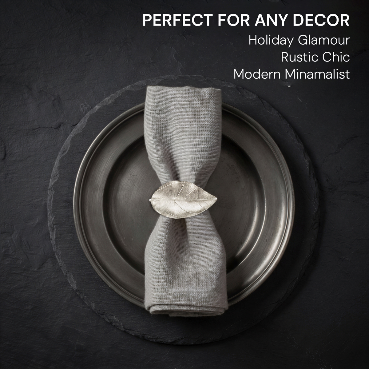 A silver metal plate with a napkin ring and a white napkin neatly folded on it, placed on a dark surface.