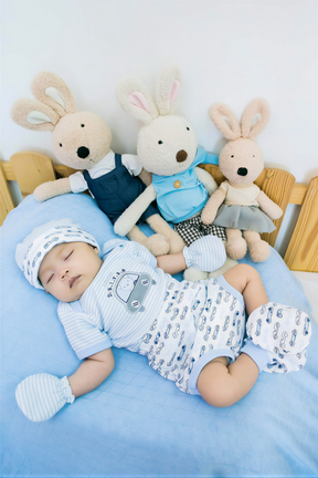 A baby is peacefully sleeping on a bed, surrounded by three stuffed rabbits.