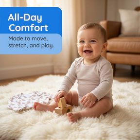 A smiling baby sitting on a white rug, holding a wooden block, with a blue banner above the image that reads "All-Day Comfort Made to move, stretch, and play."