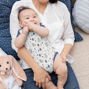 A woman is holding a baby in her lap, with a stuffed animal nearby.