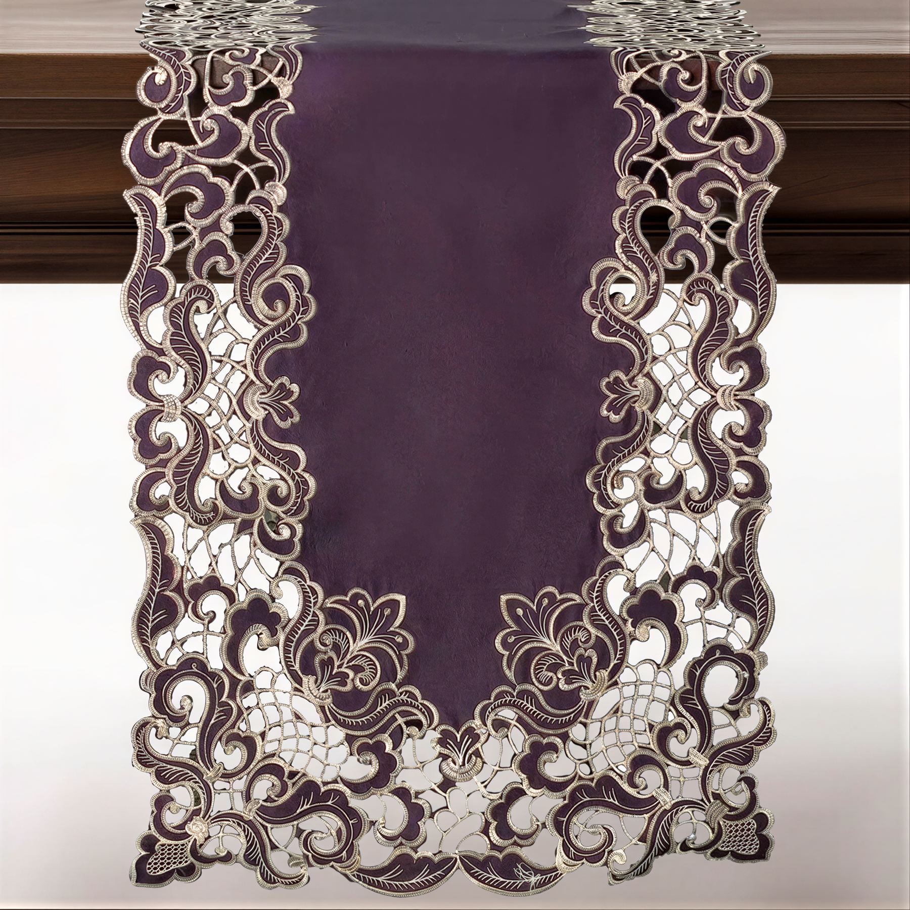 a purple table runner with an intricate, lace-like design. The design is predominantly purple and white, with a floral pattern that adds a touch of elegance to the runner. The runner is hanging on a wooden surface, creating a visually appealing and decorative display.