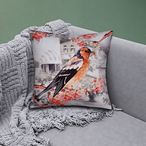 A decorative throw pillow with a colorful bird image on it, resting on a gray couch.