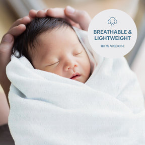 A newborn baby is wrapped in a soft white blanket, with hands gently cradling the baby's head.